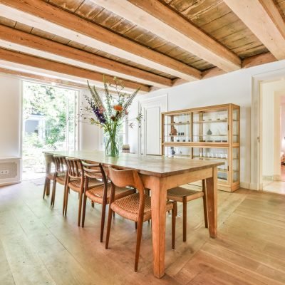 Wooden dining table with chairs under ceiling with wooden beams in cozy country room of house